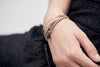 A close up of a model wearing a selection of Pyrrha bracelets including our Precious Stone 14K Gold Polished Bangle