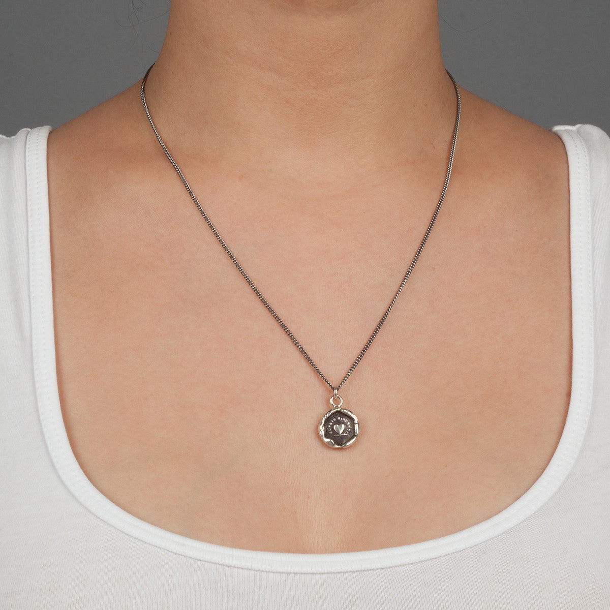 A close up of a model wearing Pyrrha's Oxidized Silver Always Sincere talisman.