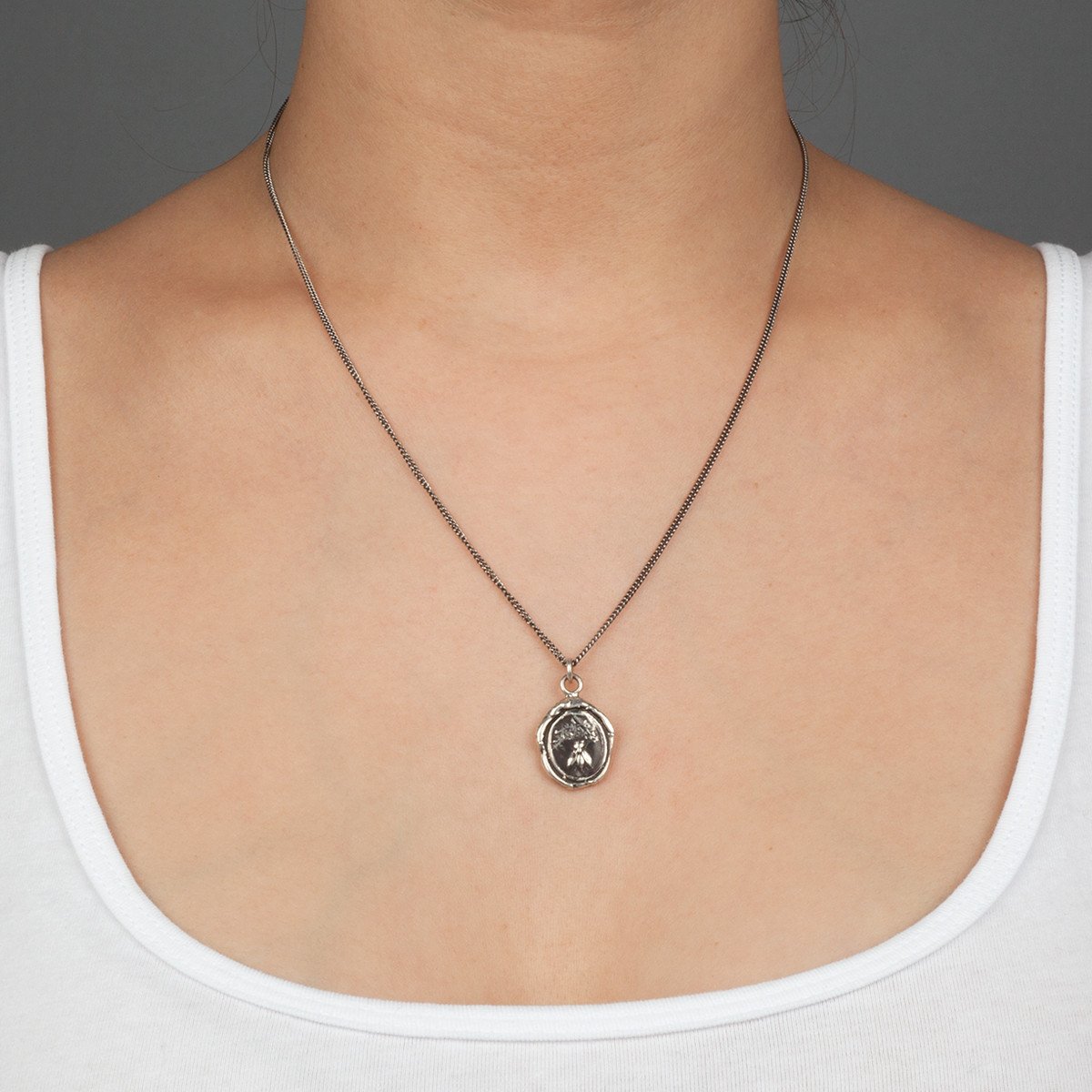 A close up of a model wearing Pyrrha's Oxidized Silver Tireless talisman.